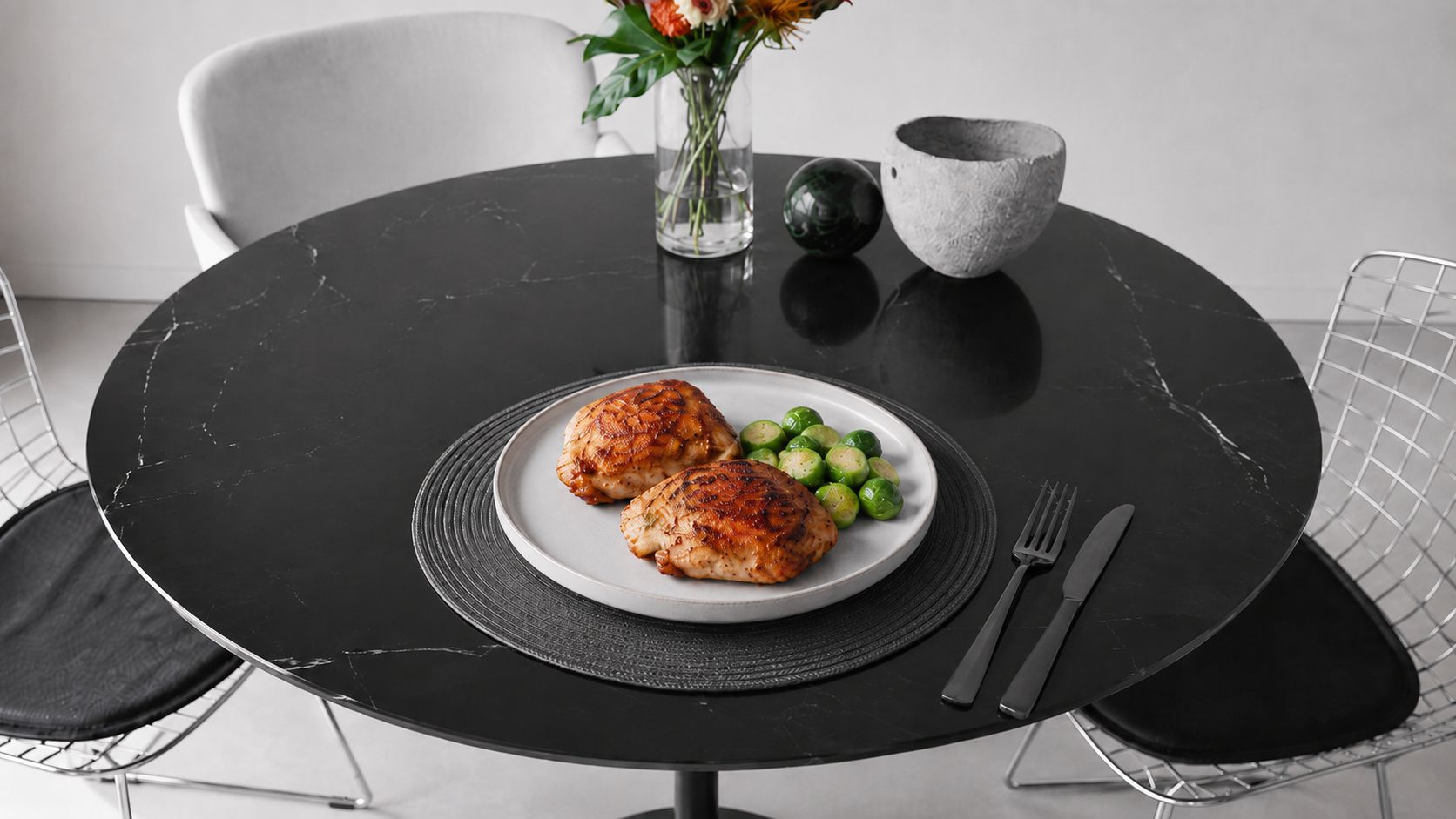 Golden-brown crispy air fryer chicken thighs on a white plate, skin deeply caramelized, garnished with fresh herbs, with a small dish of dipping sauce on the side