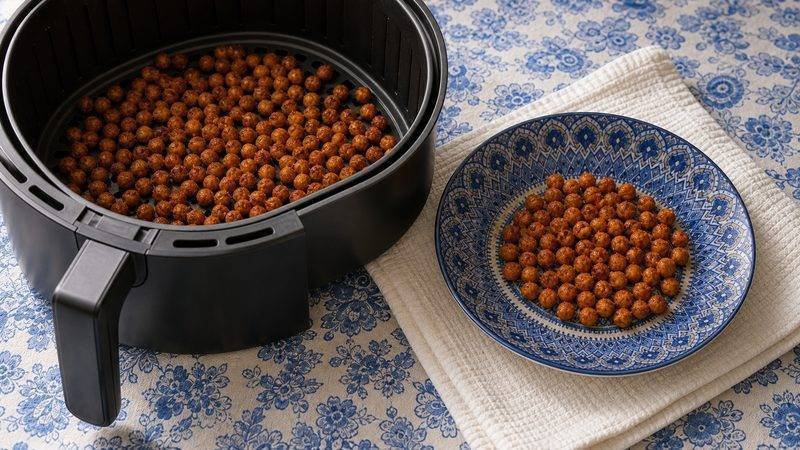 Crispy seasoned chickpeas in the air fryer basket beside a serving bowl