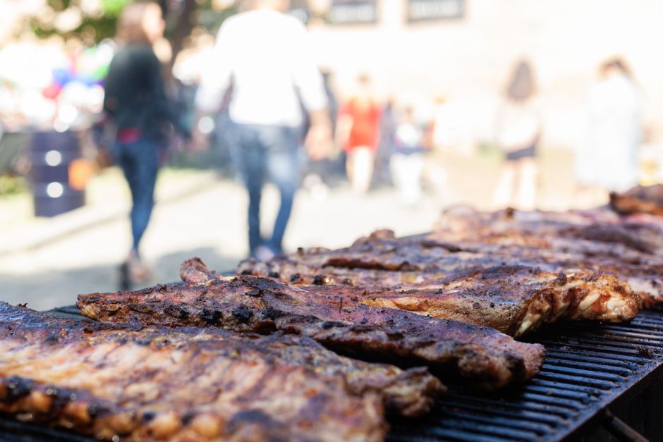 A rack of glazed baby back ribs sliced and arranged on a wooden cutting board with barbecue sauce and fresh herbs