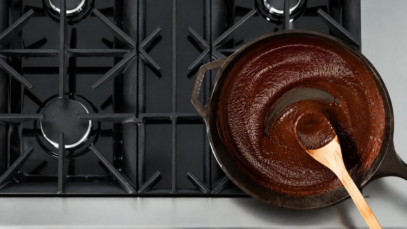 Dark chocolate roux in a cast iron skillet with a wooden spoon leaving a trail