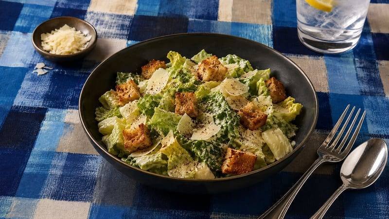 A large bowl of classic caesar salad with crispy homemade garlic croutons, shaved parmesan, and romaine lettuce coated in creamy homemade caesar dressing