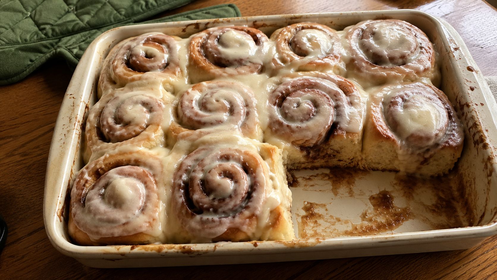 Freshly baked homemade cinnamon rolls in a pan, topped with thick cream cheese frosting melting into the warm, spiral layers