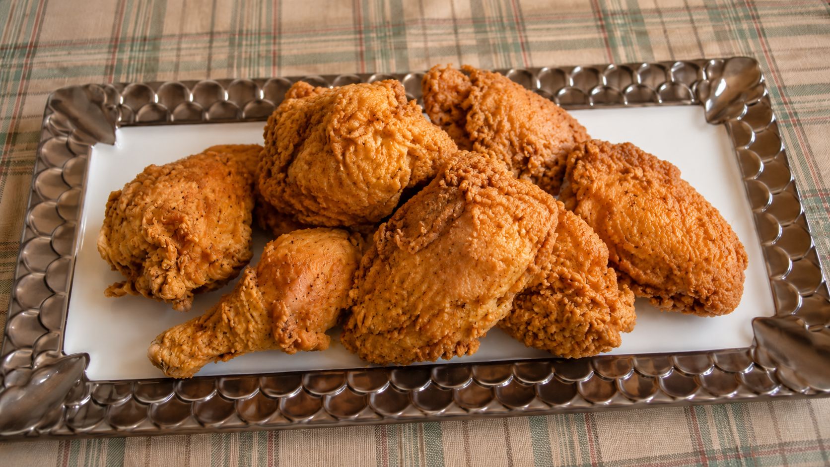 A platter of golden-brown Southern buttermilk fried chicken with shatteringly crisp crust, served on a white oval platter with a wire rack visible in the background