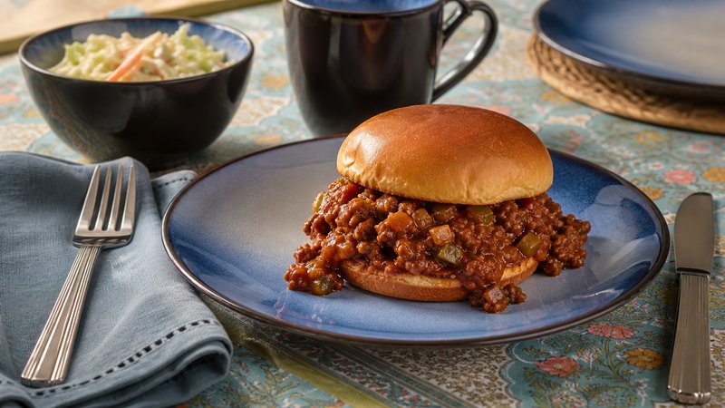 A messy sloppy joe on a toasted bun, sauce dripping down the sides, ready to eat with a napkin nearby