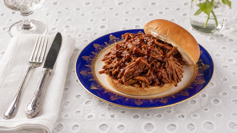 Shredded pulled pork piled high on a hamburger bun, glistening with BBQ sauce