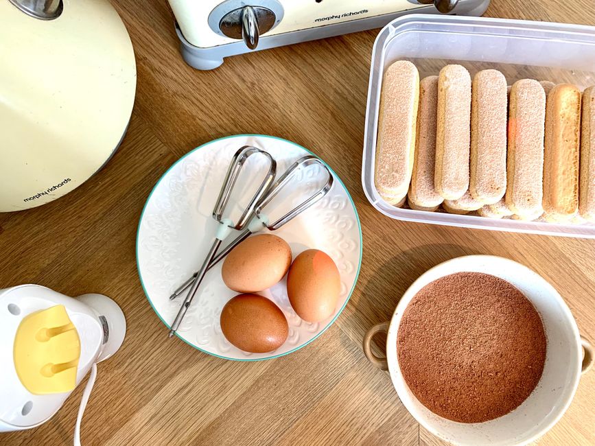 Classic tiramisu served in a white ceramic dish, showing distinct layers of espresso-soaked ladyfingers and mascarpone cream, dusted with dark cocoa powder