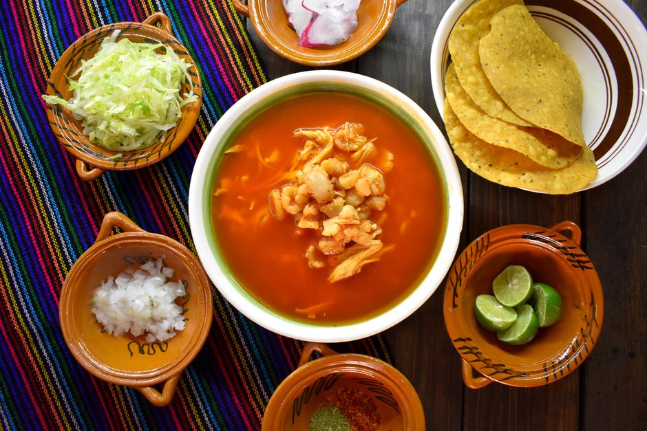 A rustic bowl of homemade tortilla soup topped with crispy tortilla strips, shredded cheese, sour cream, and sliced avocado, with a lime wedge on the side