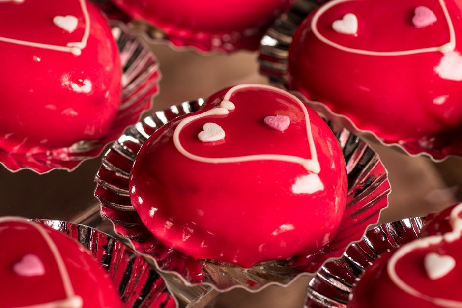 Two molten chocolate lava cakes on white plates dusted with powdered sugar and topped with fresh raspberries, photographed on a dark wood surface with a fork breaking into one to reveal the flowing chocolate center