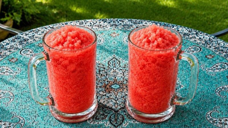 Two clear mugs filled with bright pink Watermelon Granita on a patterned outdoor table